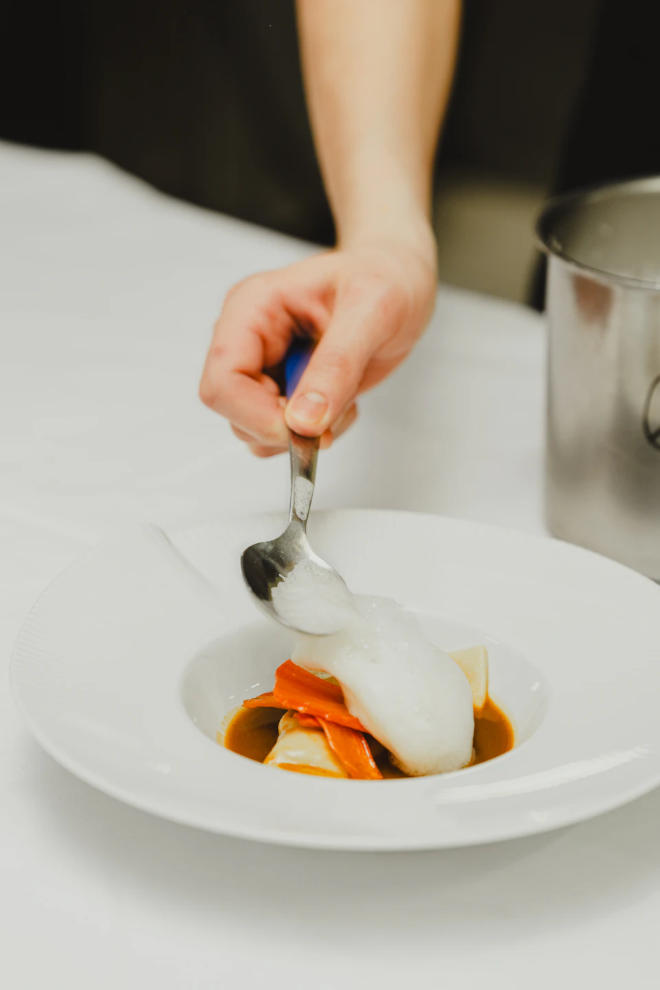Hand holding silver spoon poised to dip into creamy sauce-filled white bowl