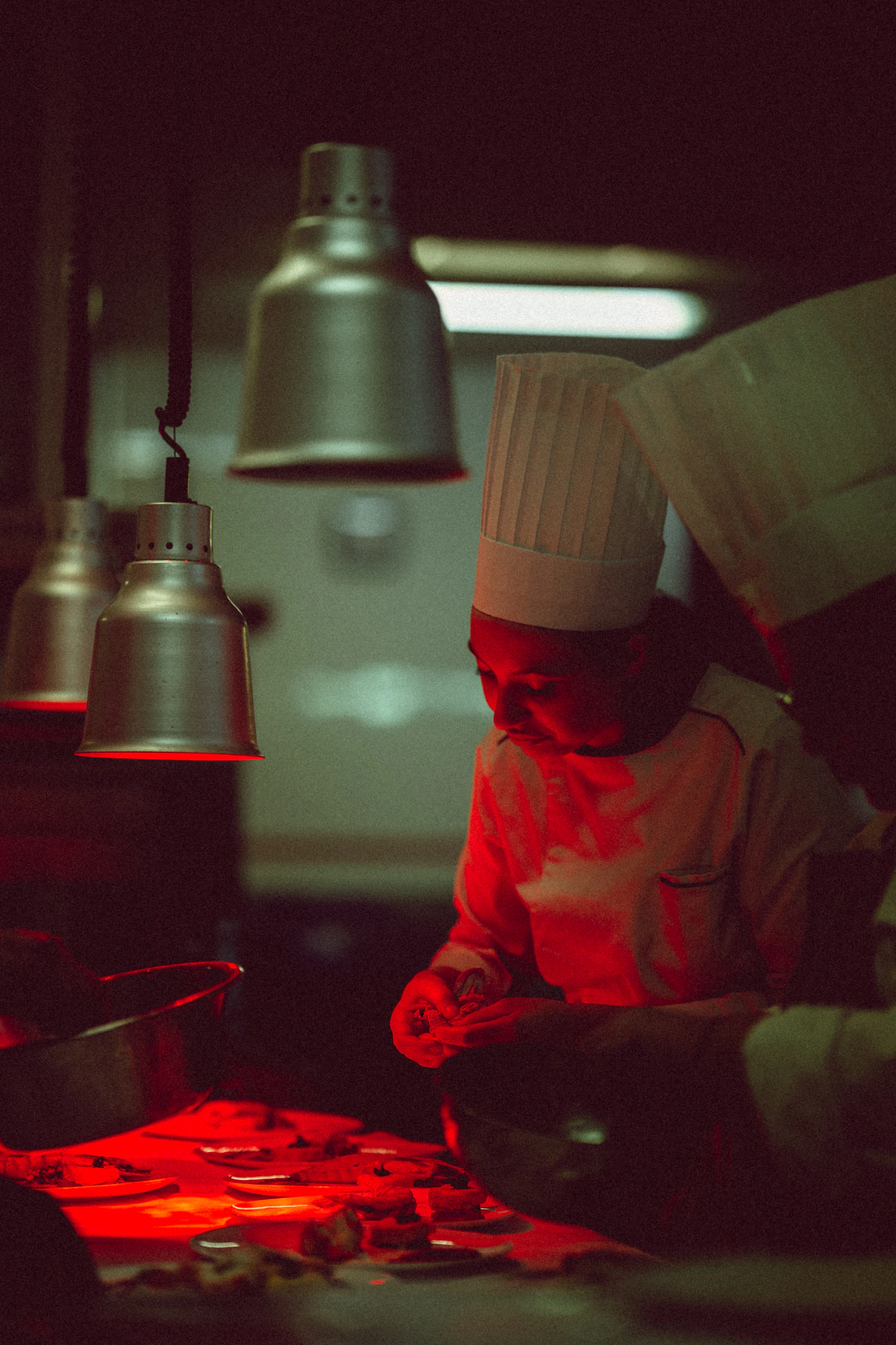 A chef plating beneath warm red heat lamps at night