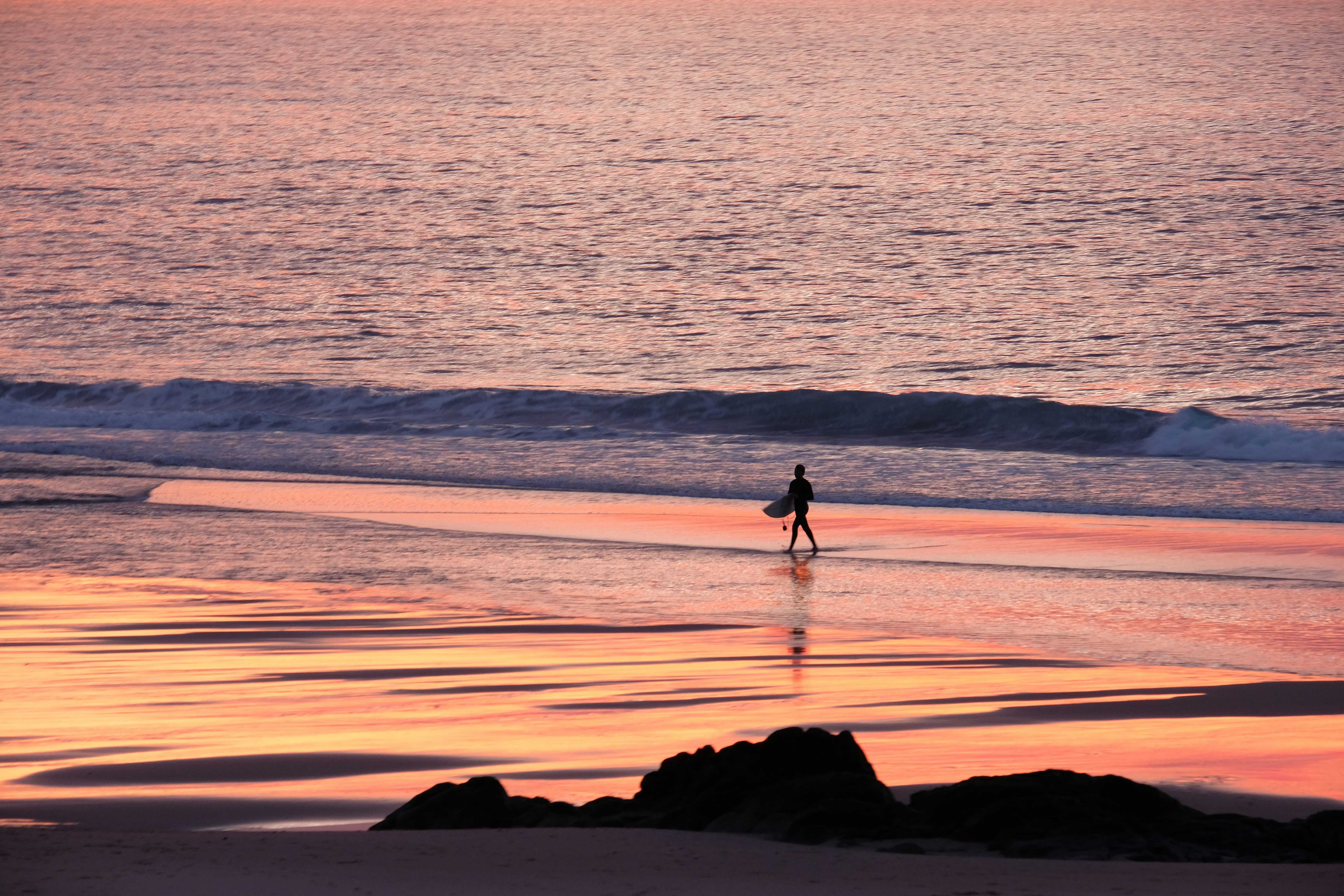 uma pessoa andando na praia com uma prancha de surf