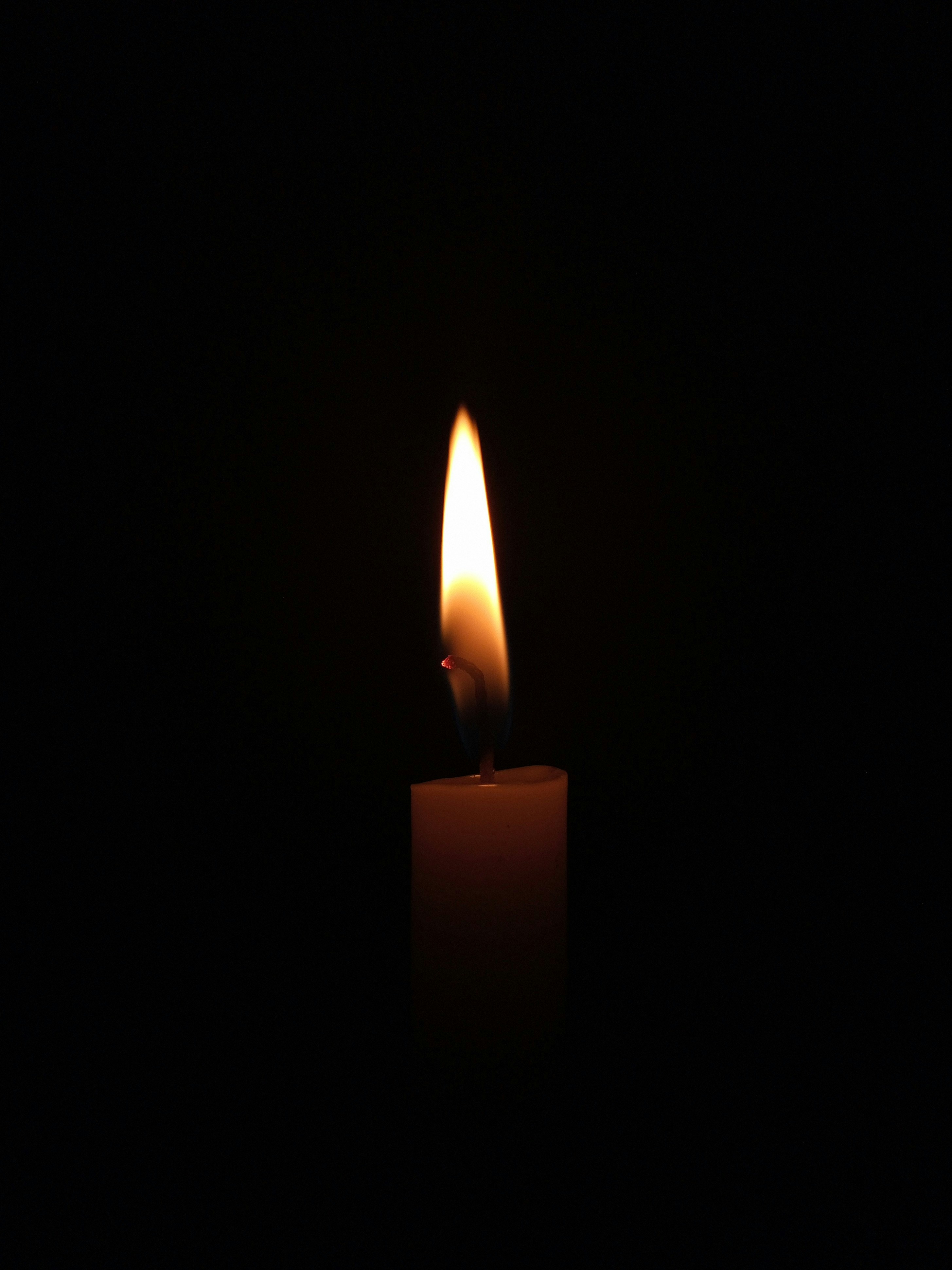 Single candle flame in darkness, warm amber light, intimate and sacred, quiet persistence