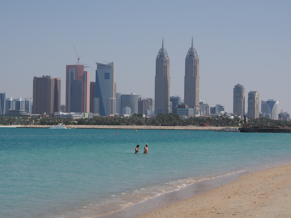 a beach with people in the water and a city in the background