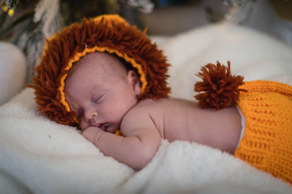 a baby wearing a lion costume sleeping on a blanket