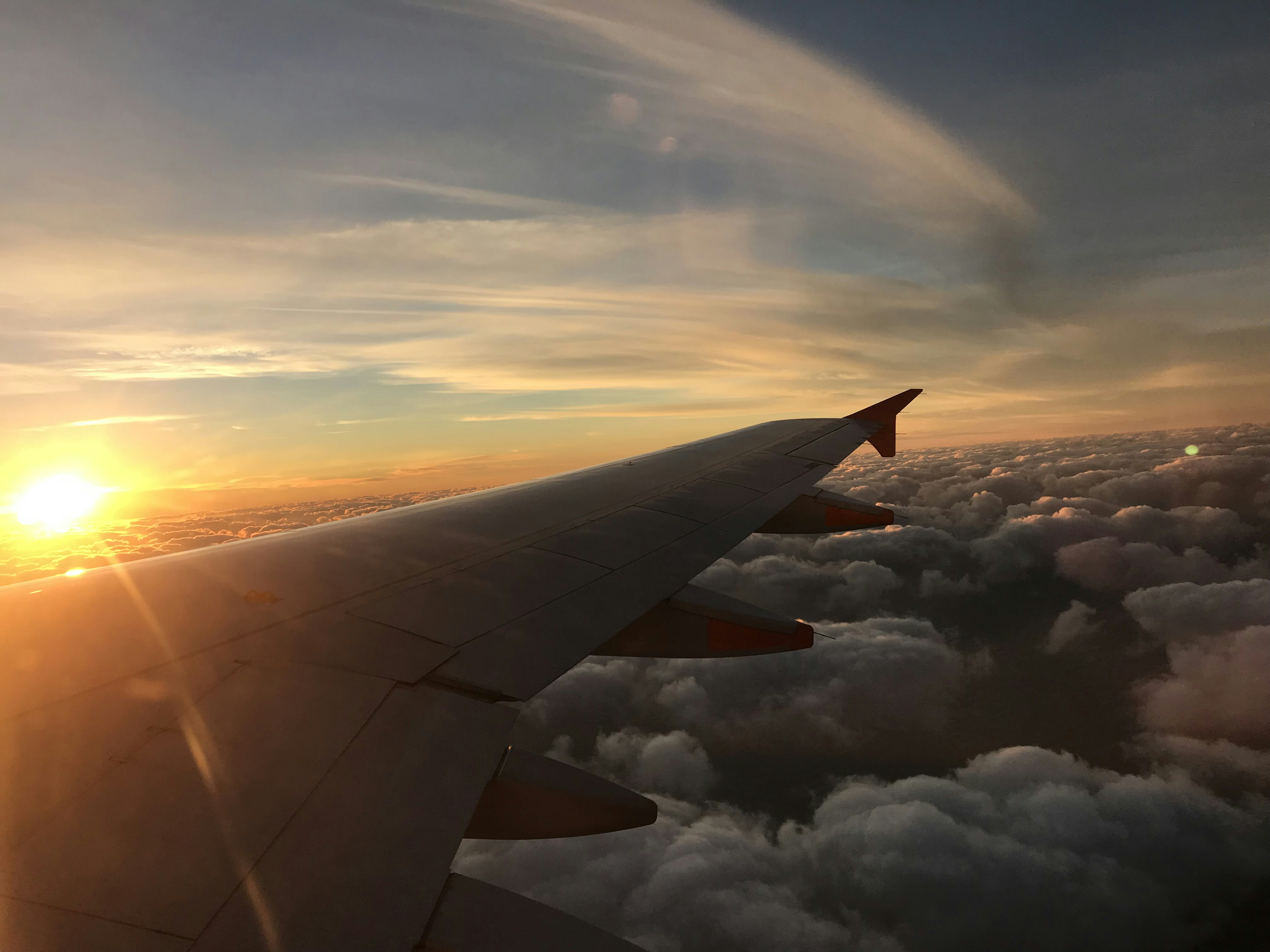Airplane wing above clouds during golden hour flight with warm orange sunset glow