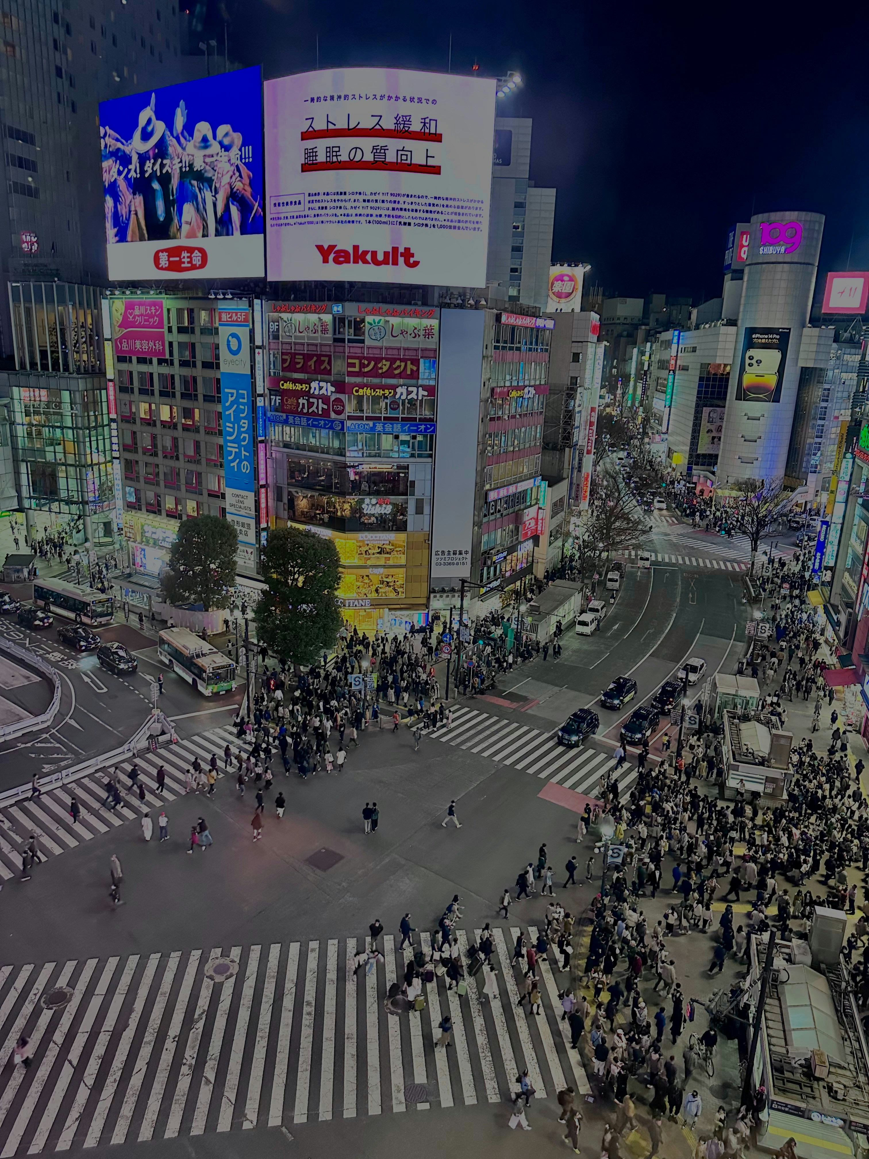 Tokyo Shibuya crossing at night with neon signs and hundreds of people crossing in all directions under bright artificial light