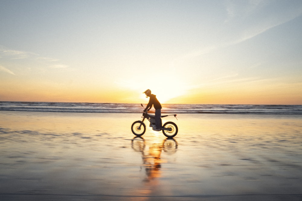 une personne faisant du vélo sur la plage au coucher du soleil