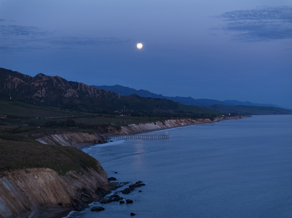 a full moon setting over the ocean with mountains in the background