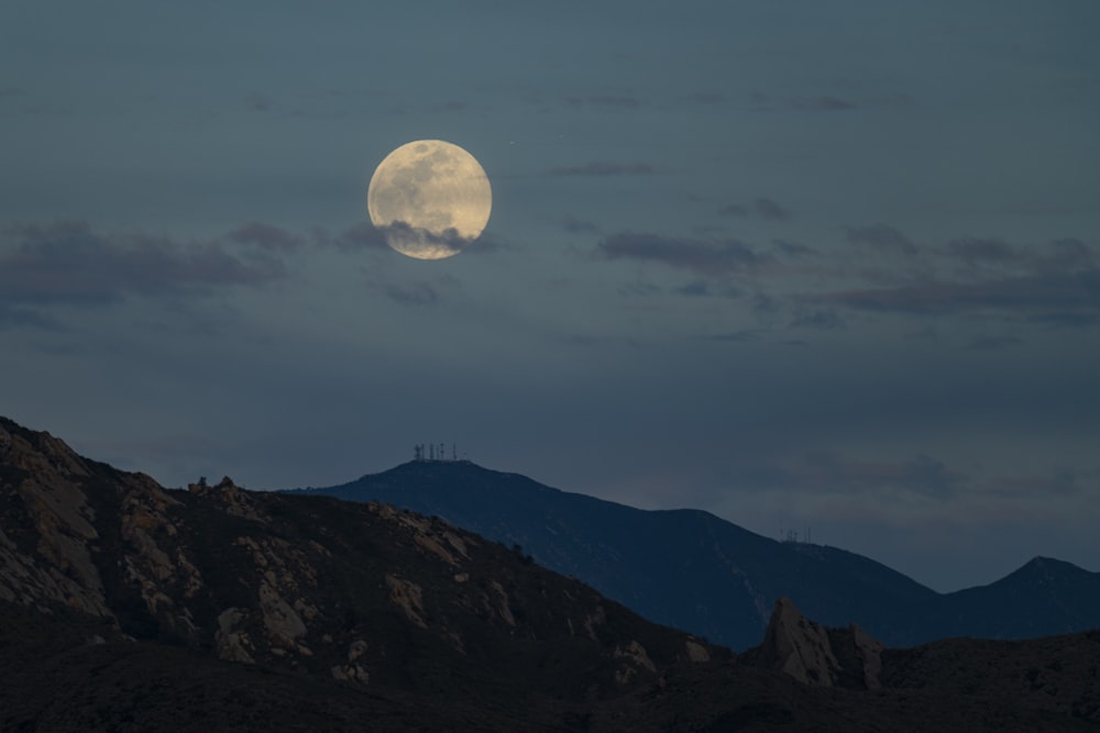 a full moon rising over a mountain range