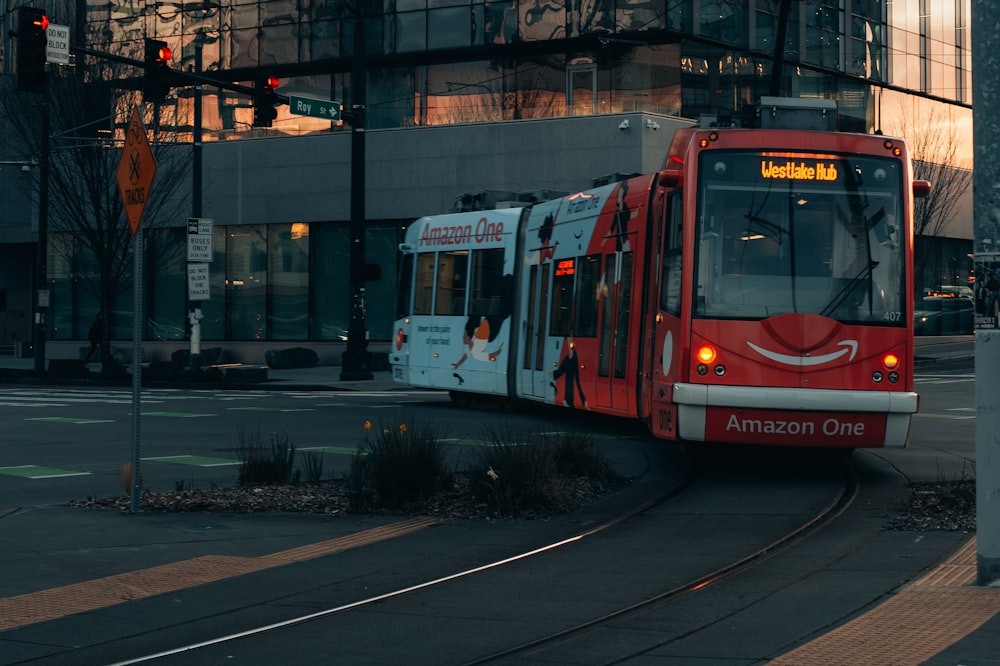 a red and white train traveling down a street next to a tall building