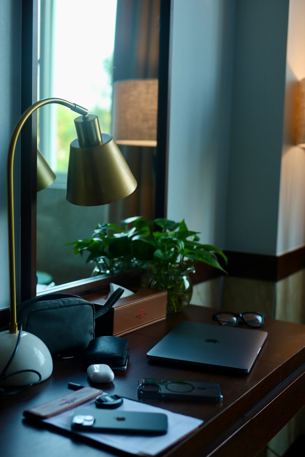 a desk with a lamp, cell phone and a laptop on it