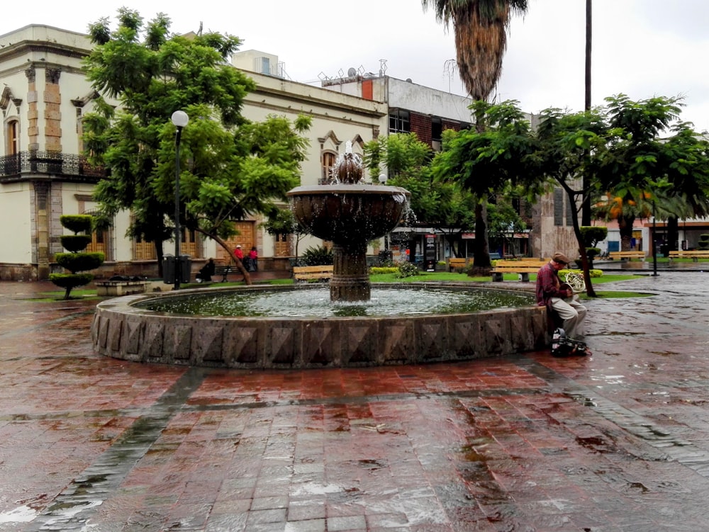 a person sitting on a bench in front of a fountain