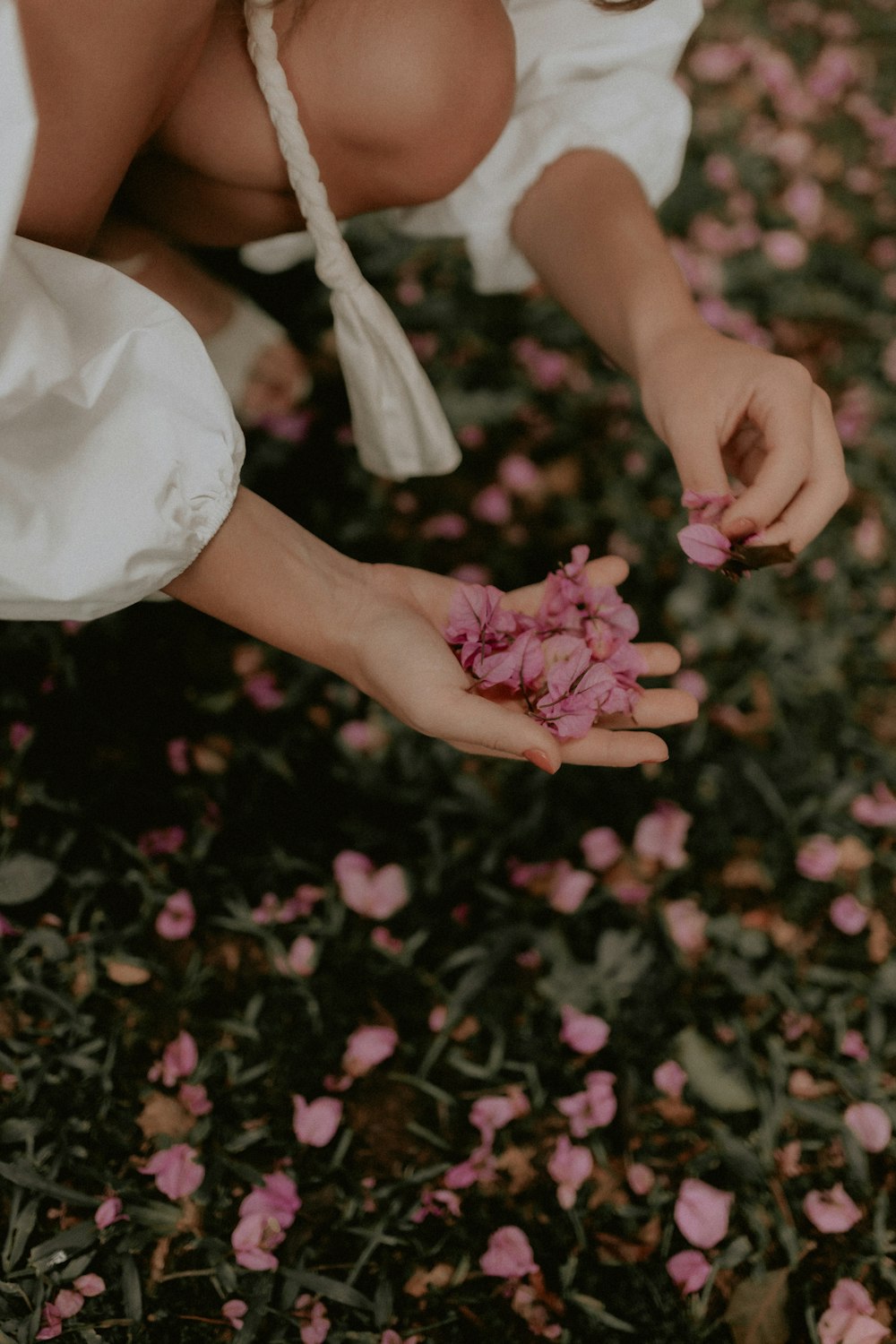 a woman kneeling down holding a bunch of pink flowers