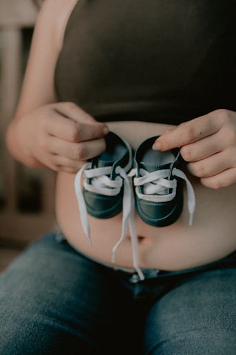 a pregnant woman holding a pair of baby shoes
