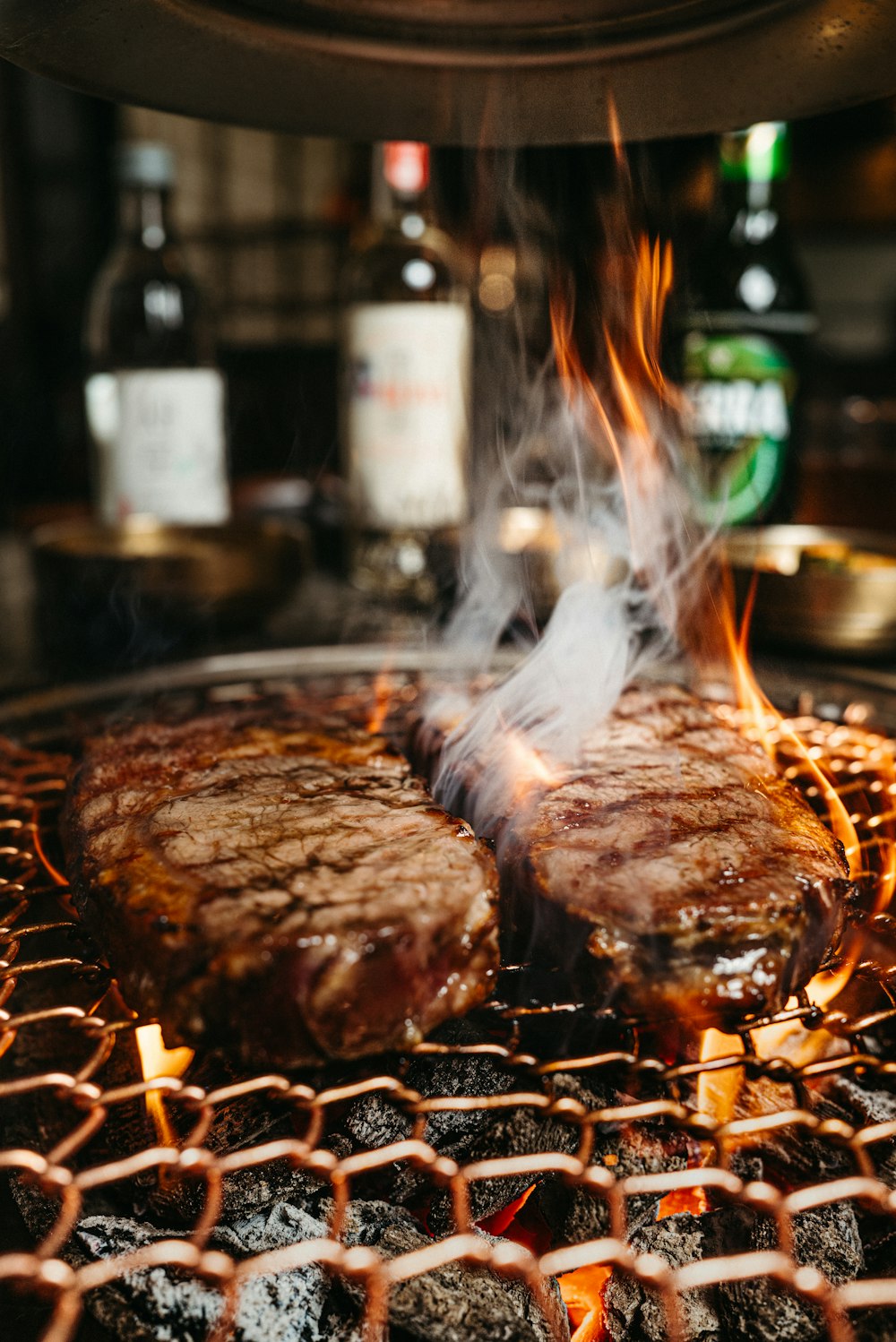 two steaks cooking on a grill with flames