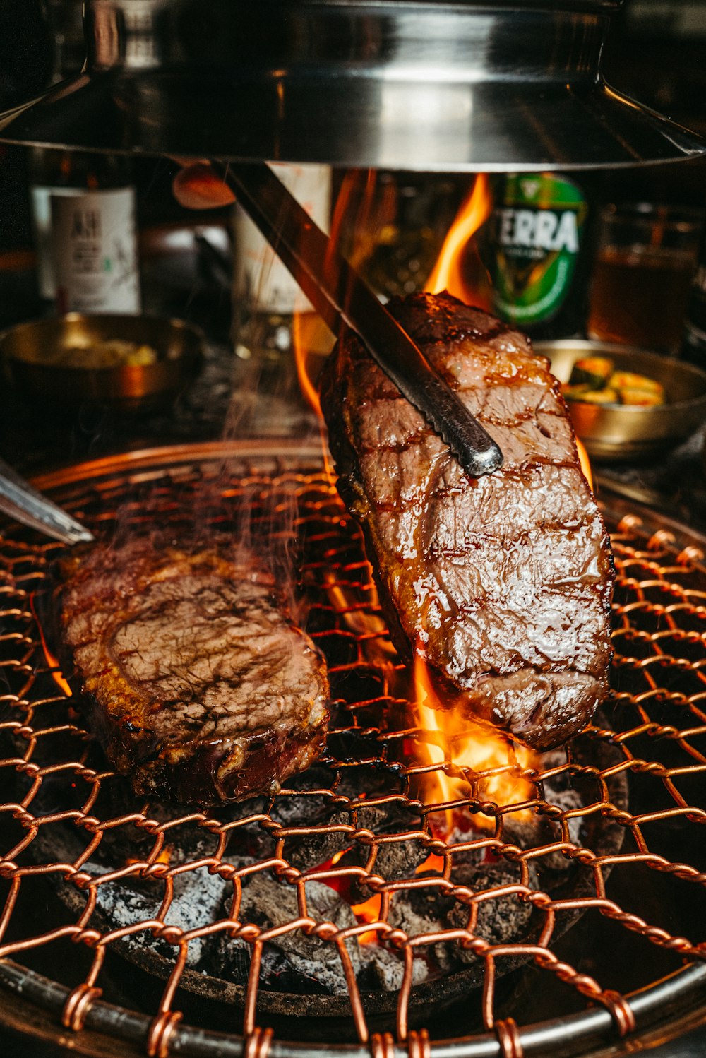 a steak being cooked on a grill with tongs