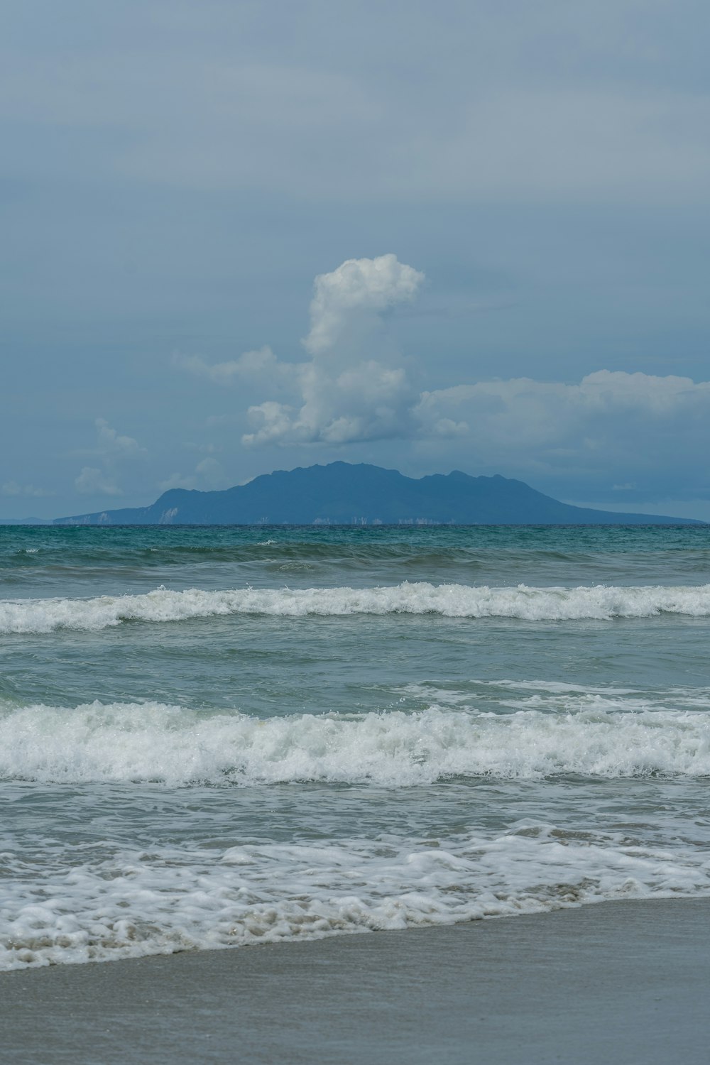 a beach with waves and a mountain in the distance
