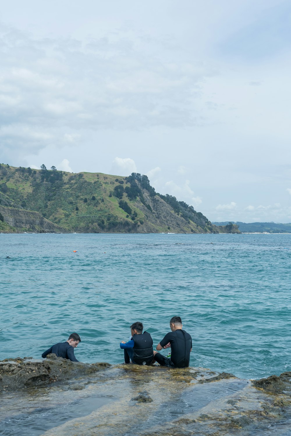 a group of people sitting on top of a rock next to the ocean