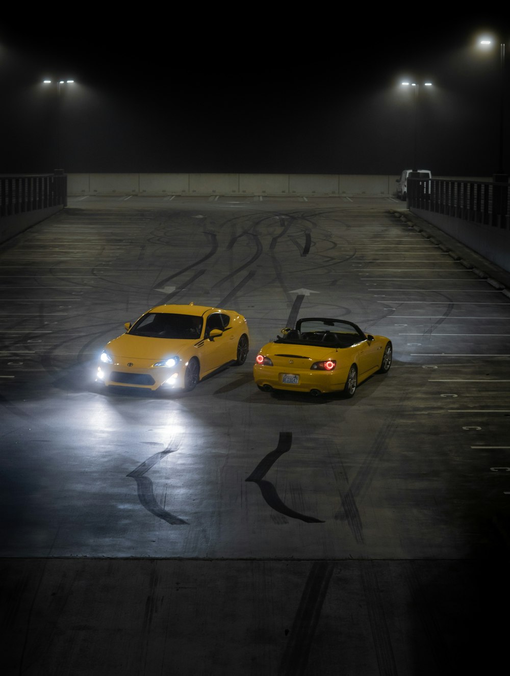 two yellow sports cars in a parking lot at night