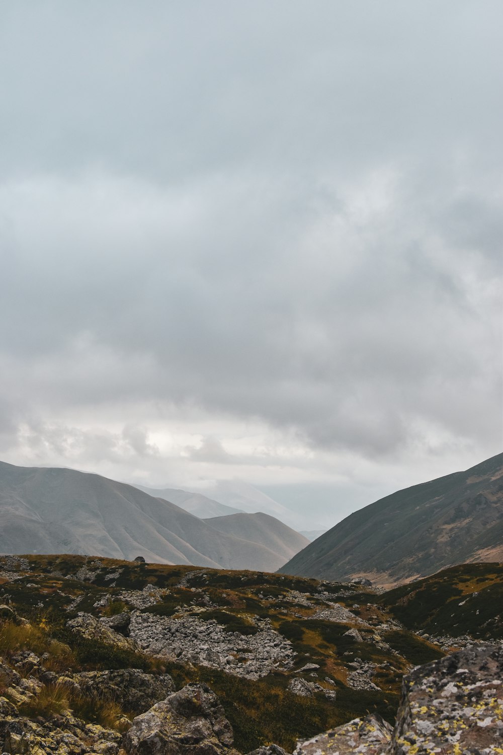 a person standing on a rocky hillside with mountains in the background