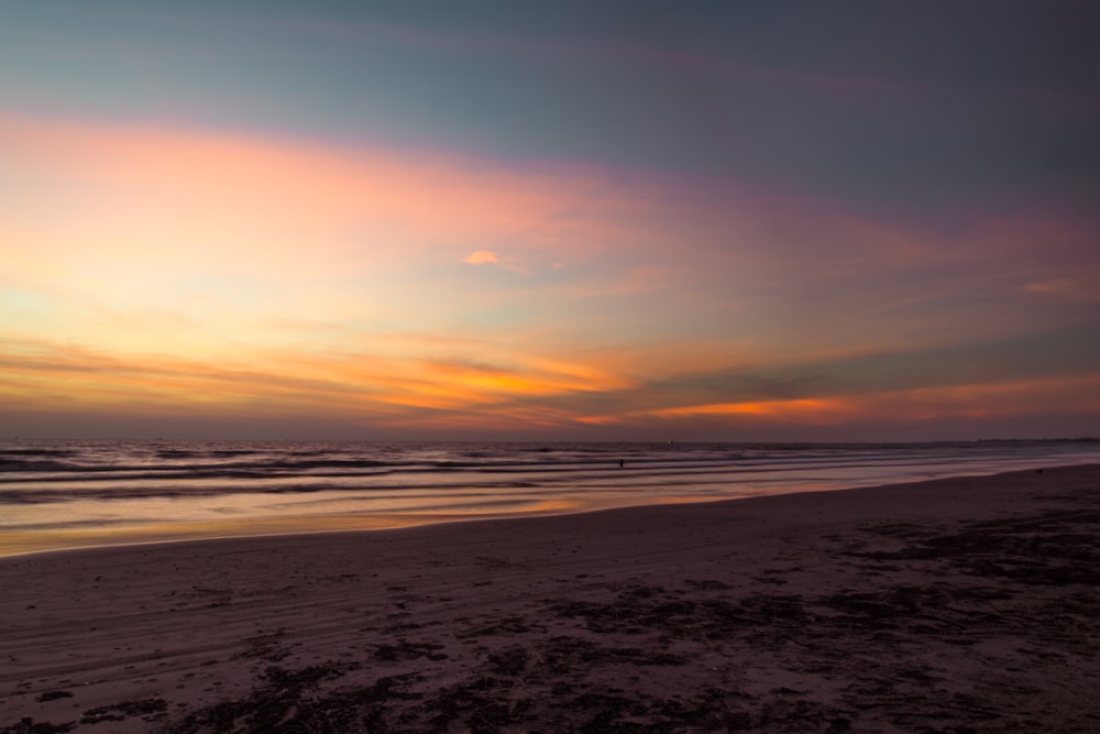 the sun is setting over the ocean on the beach