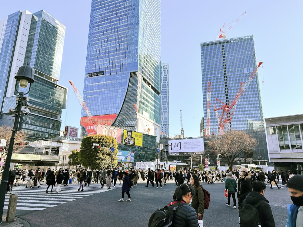 a group of people walking across a street next to tall buildings