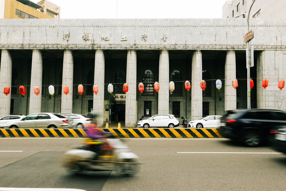 a motorcycle driving past a tall building with columns