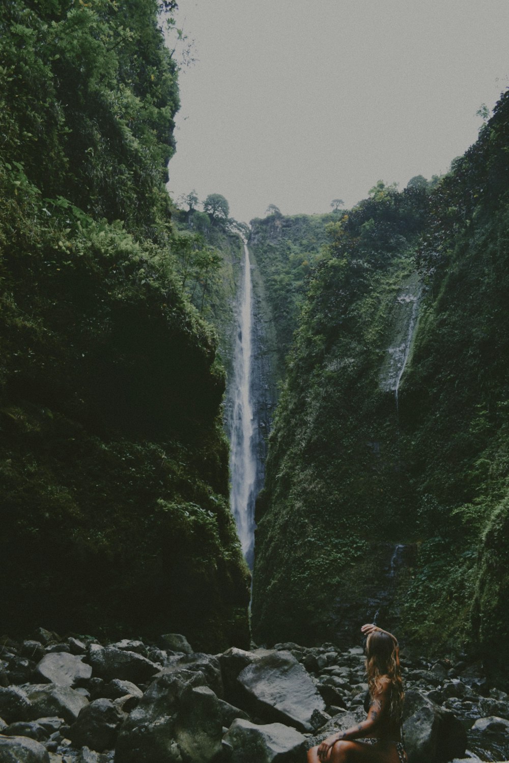 a woman sitting on rocks in front of a waterfall