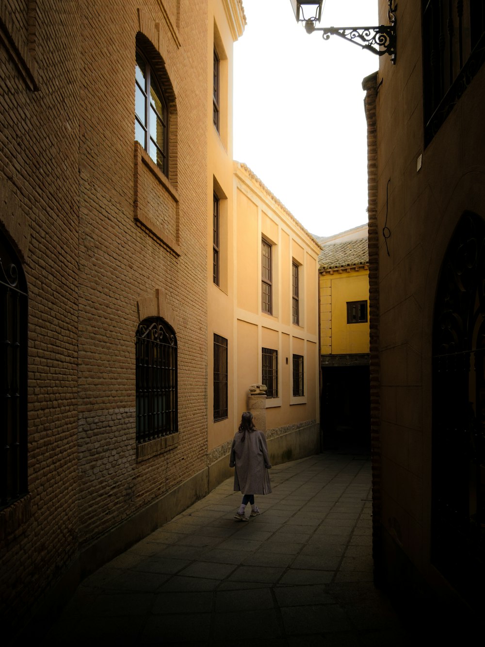 a woman walking down a street next to tall buildings