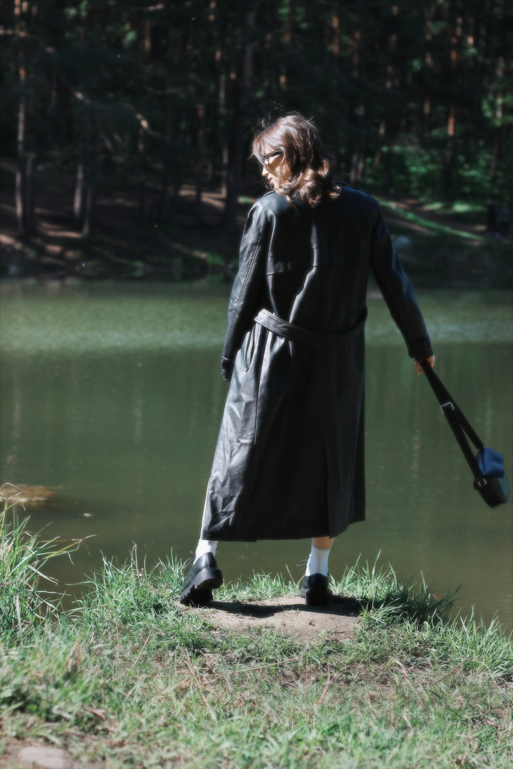 a woman in a long coat is standing by the water