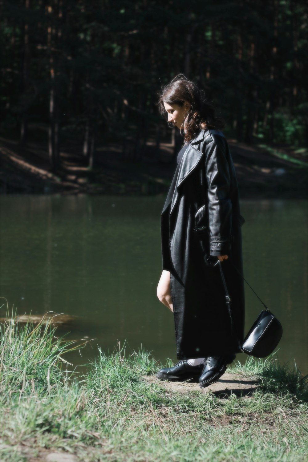 a woman in a black coat is standing by the water