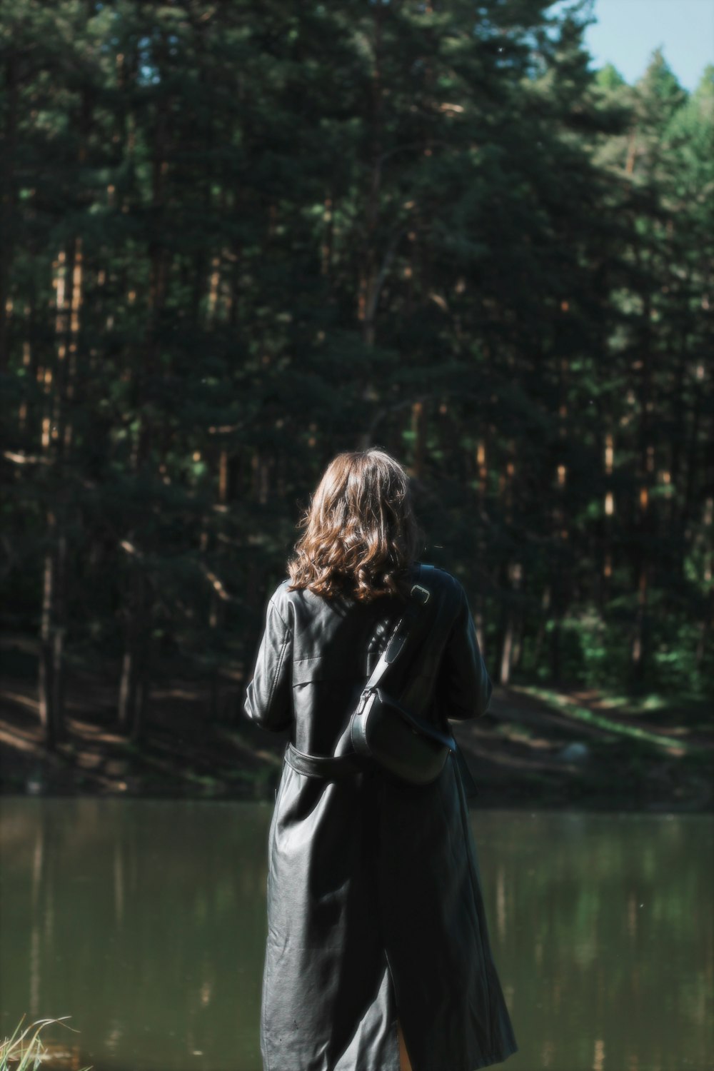 a woman in a black coat standing in front of a lake