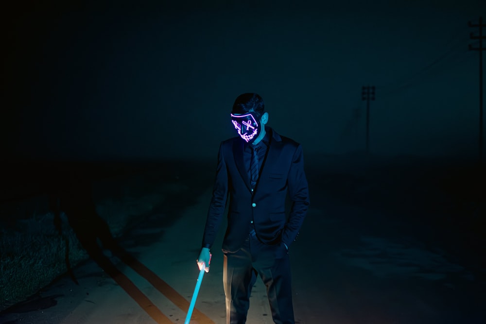 Ein Mann mit Neonmaske und einem Stock in der Hand