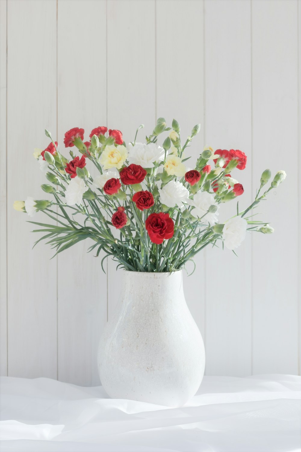 a white vase filled with red and white flowers