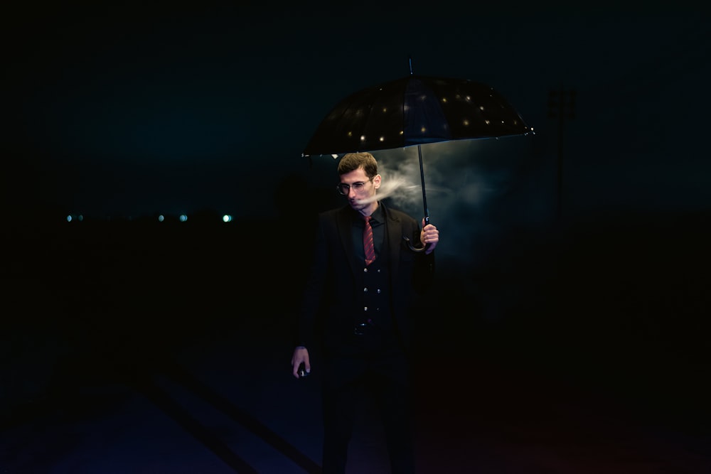 a man standing in the dark holding an umbrella