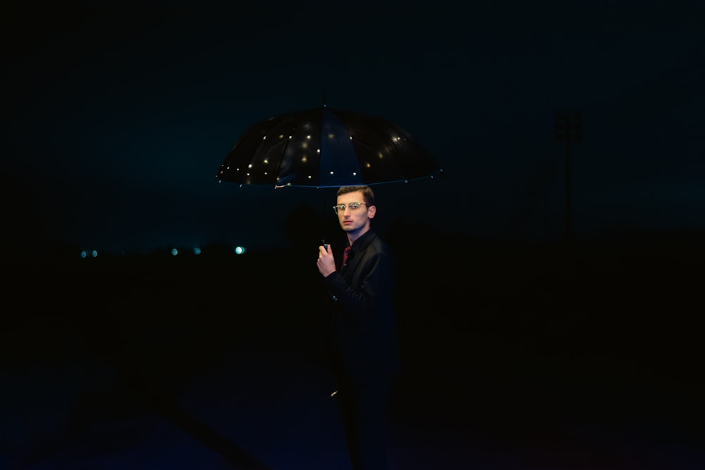 a man standing in the dark holding an umbrella