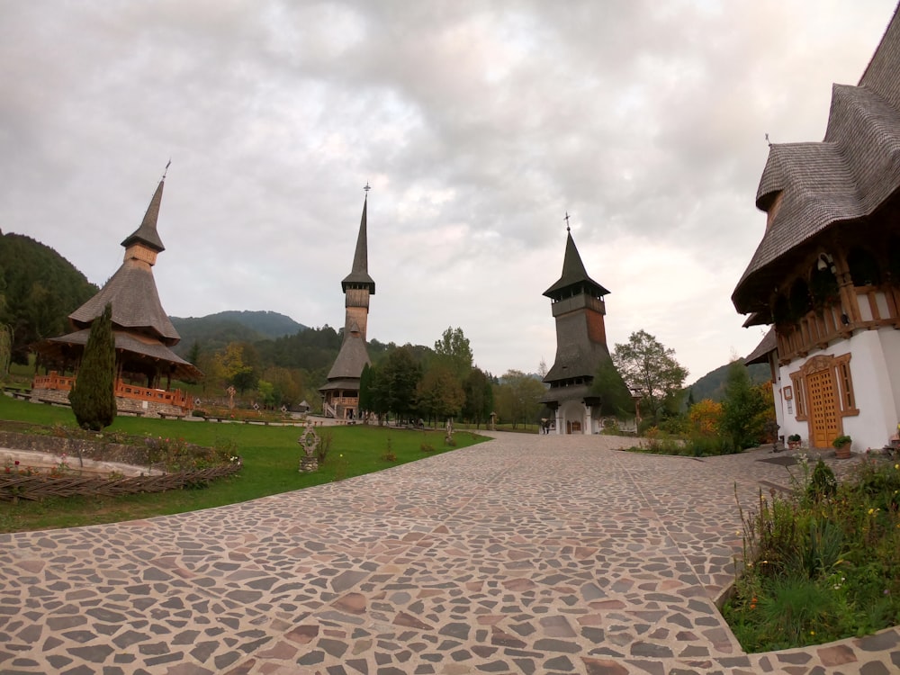 a cobblestone walkway leads to a row of thatched roofed buildings