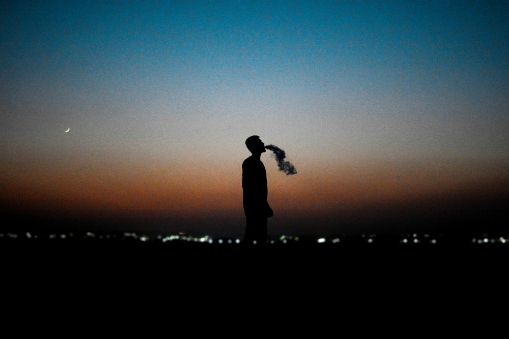 a silhouette of a man blowing smoke into the air