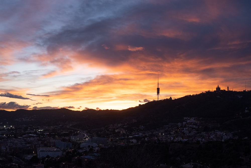 the sun is setting over a city with hills in the background