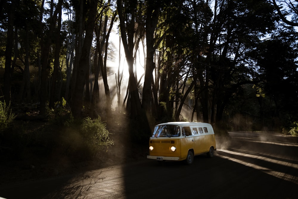 a yellow and white van driving down a road next to trees
