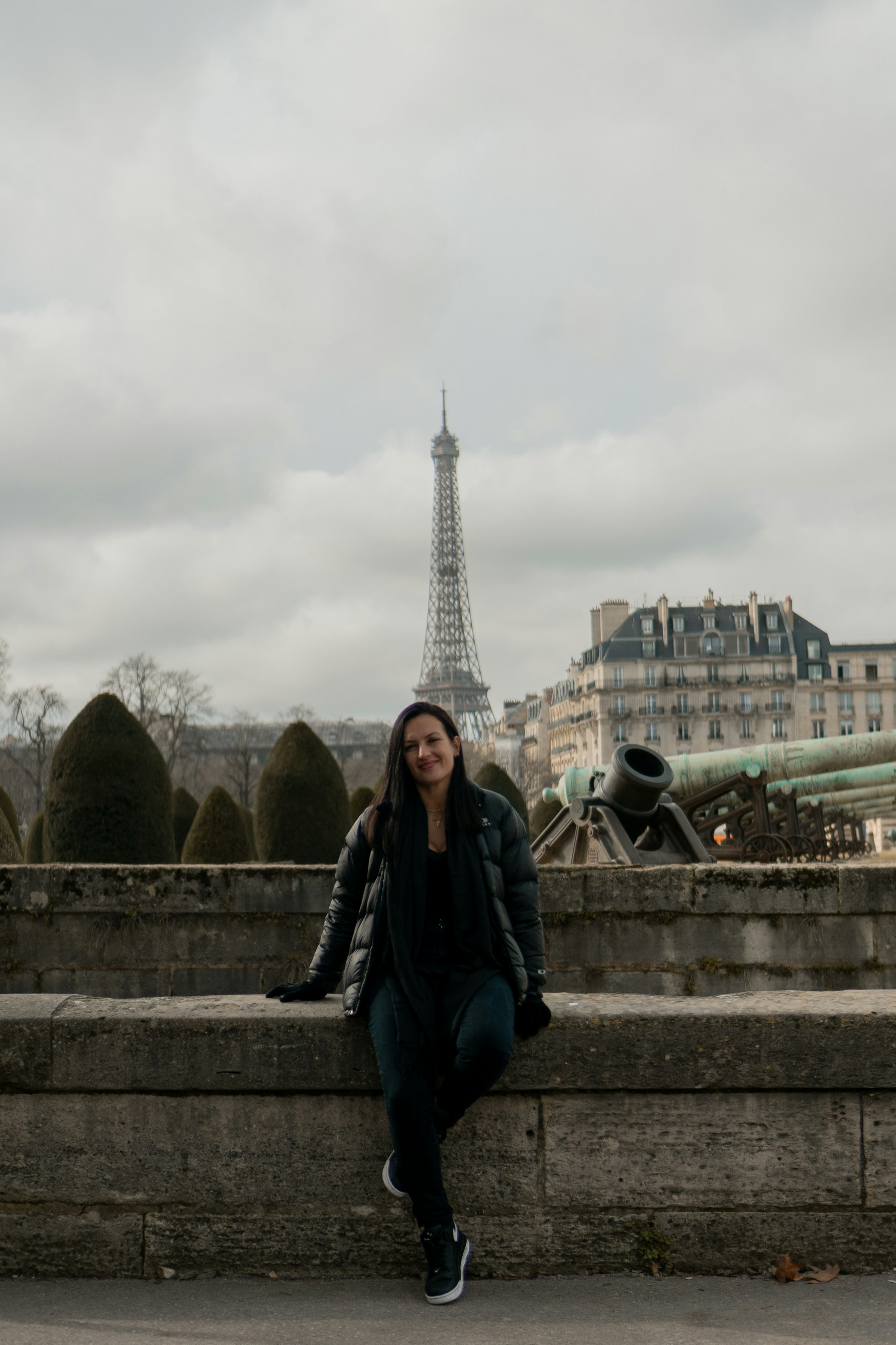 a woman sitting on a stone wall in front of the eiffel tower