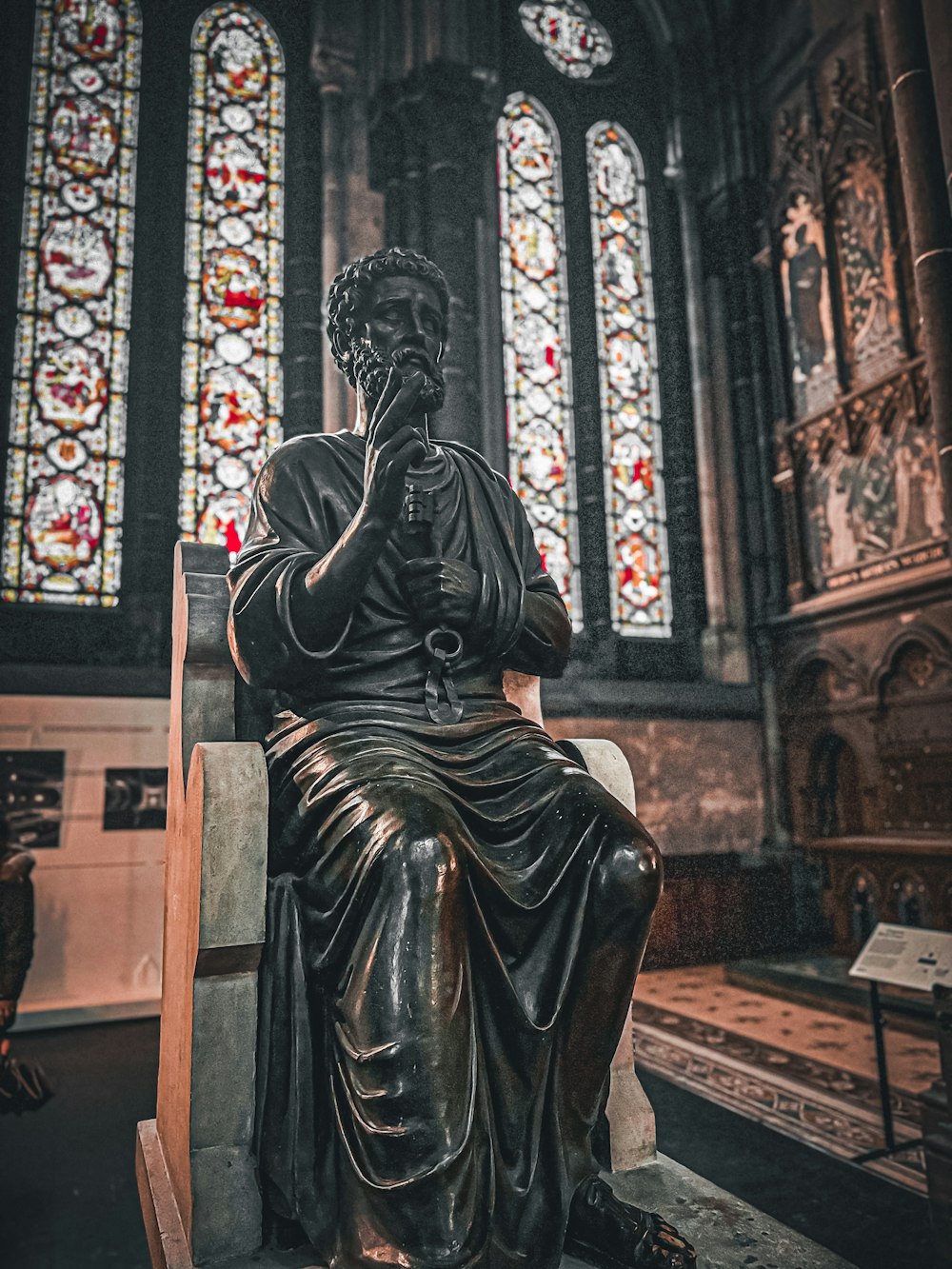 a statue of a man sitting in front of a stained glass window
