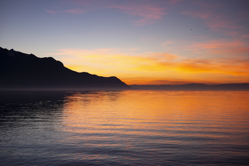 the sun is setting over the water with mountains in the background