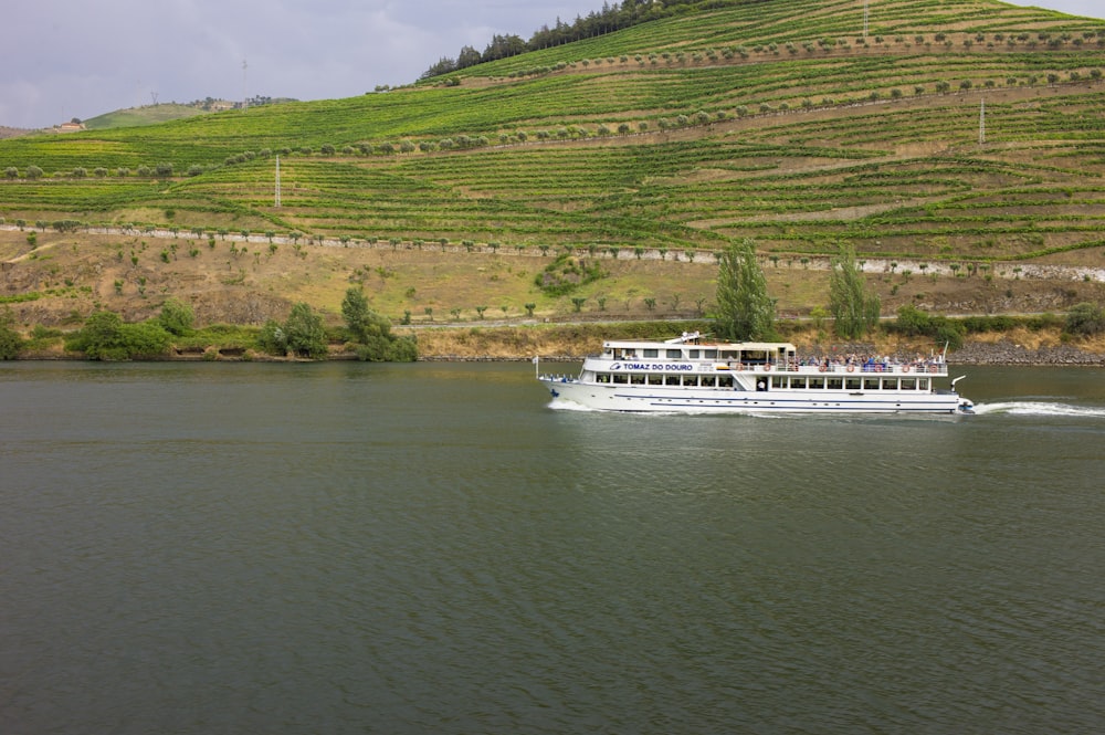 a large white boat traveling down a river next to a lush green hillside