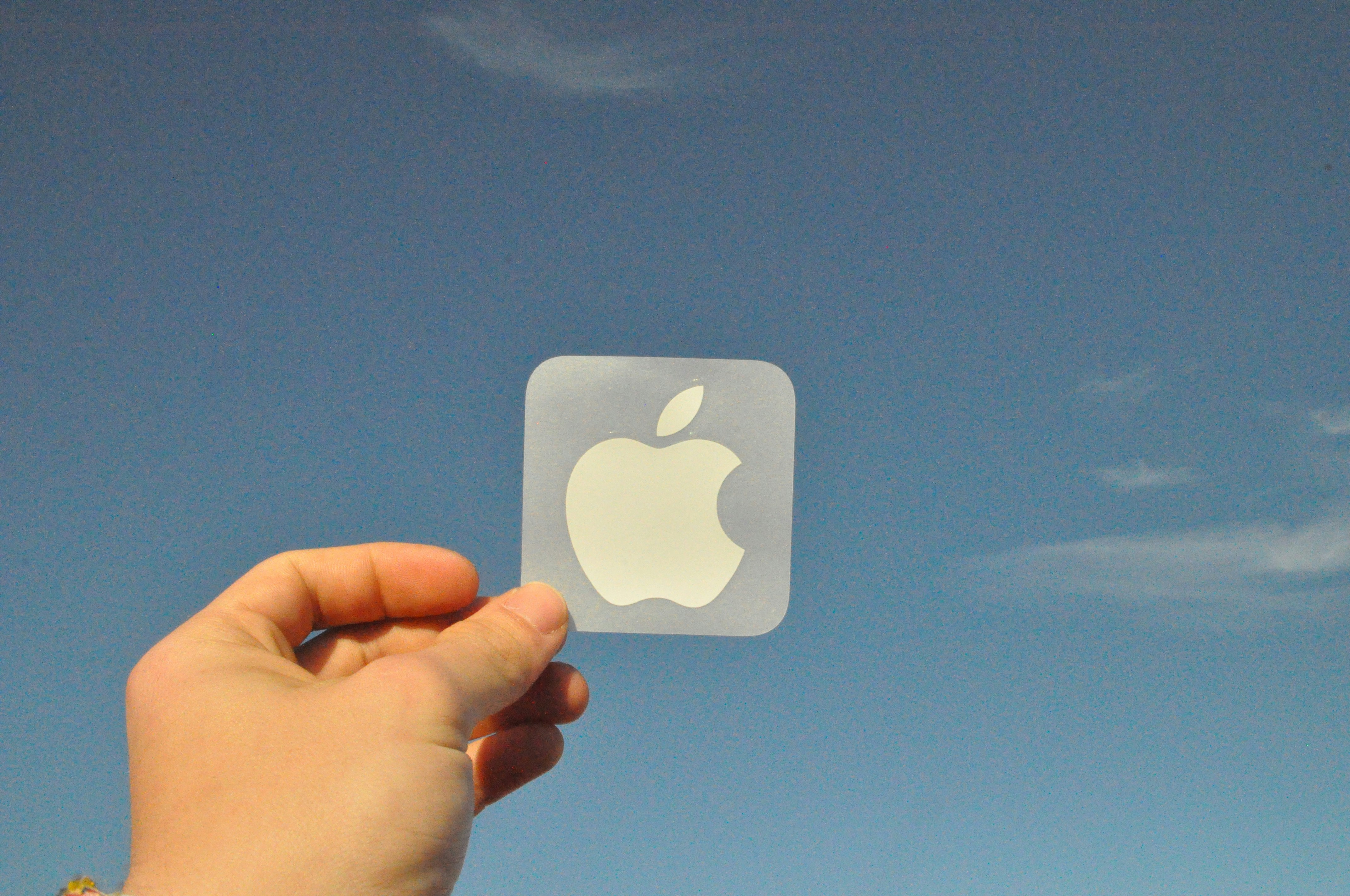 a hand holding an apple sticker in front of a blue sky