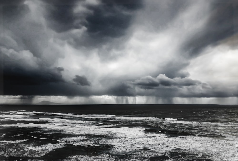 a black and white photo of storm clouds over the ocean