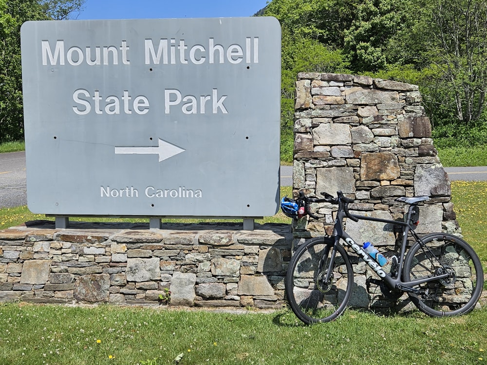 Ein Fahrrad, das neben einem Schild für den Mount Mitchell State Park geparkt ist