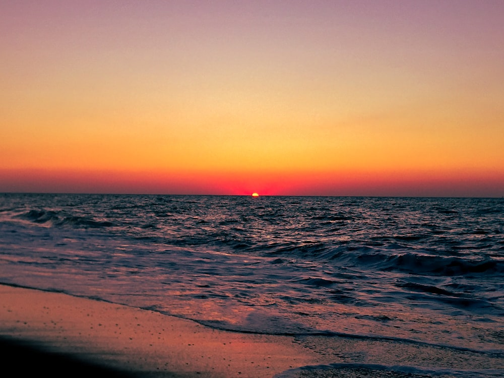 the sun is setting over the ocean at the beach