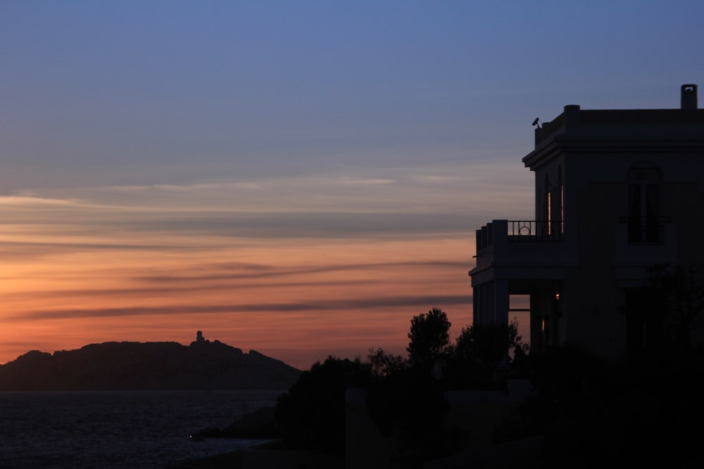 the sun is setting over the ocean with a house in the foreground