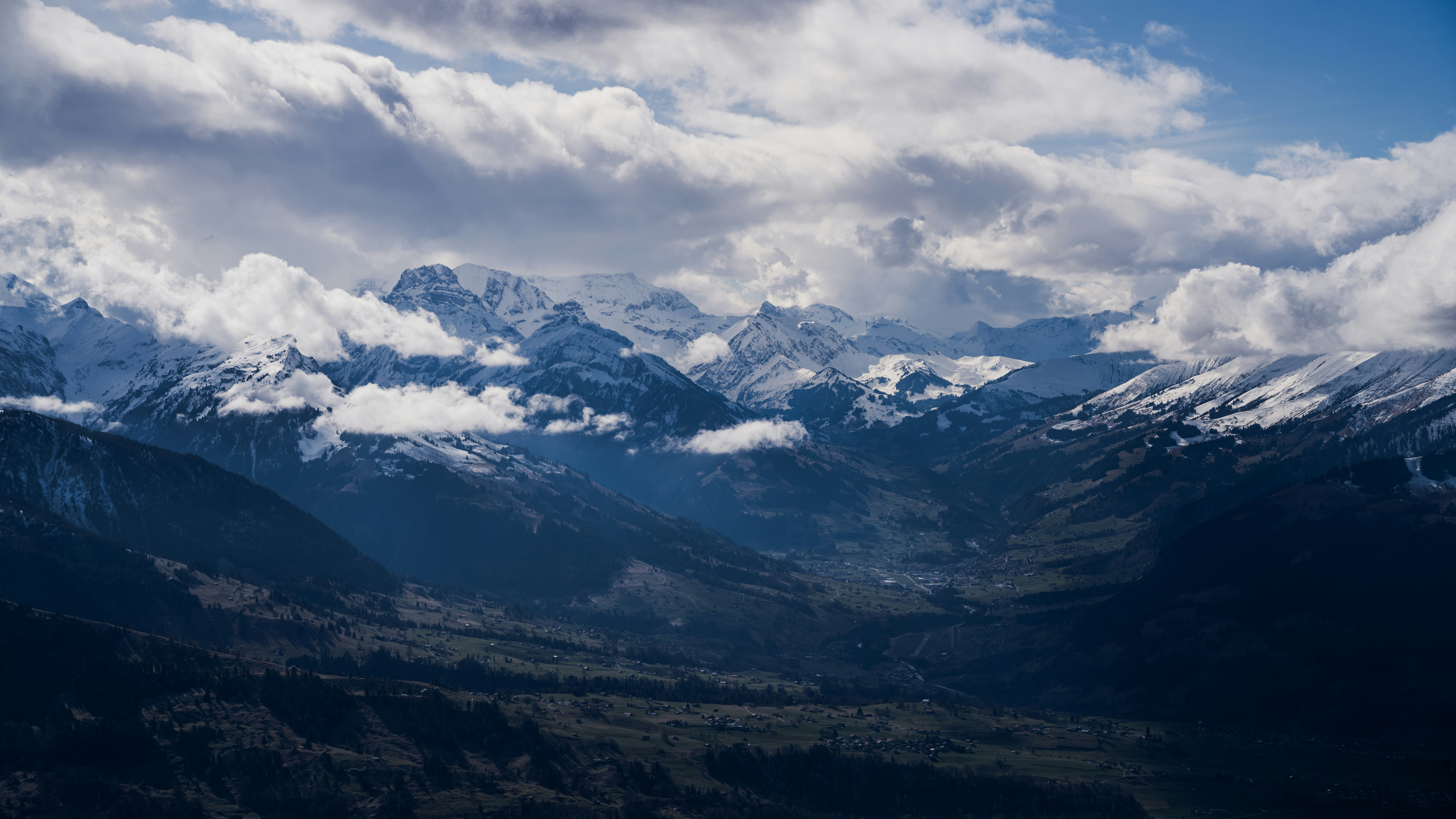 a view of a mountain range with clouds in the sky, Snow covered the Bernese Alps and the valley.