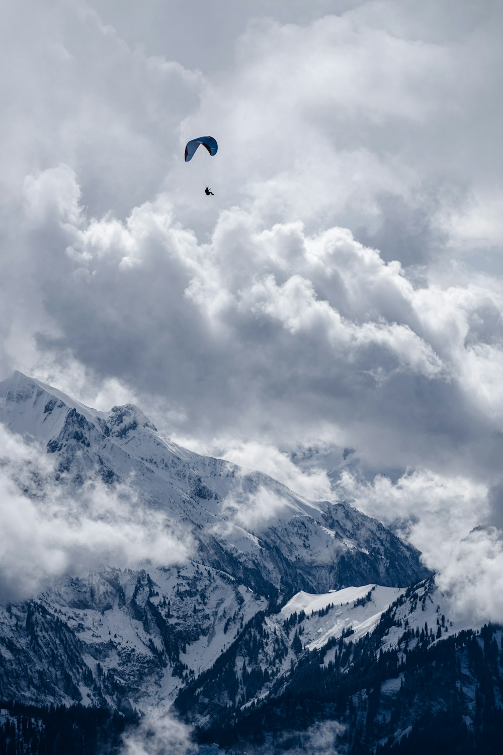 a paraglider flying over a mountain range under a cloudy sky