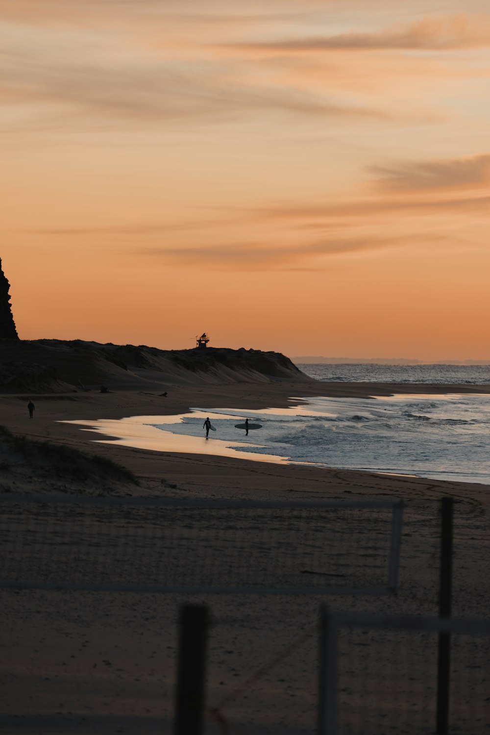 a couple of people walking on a beach at sunset